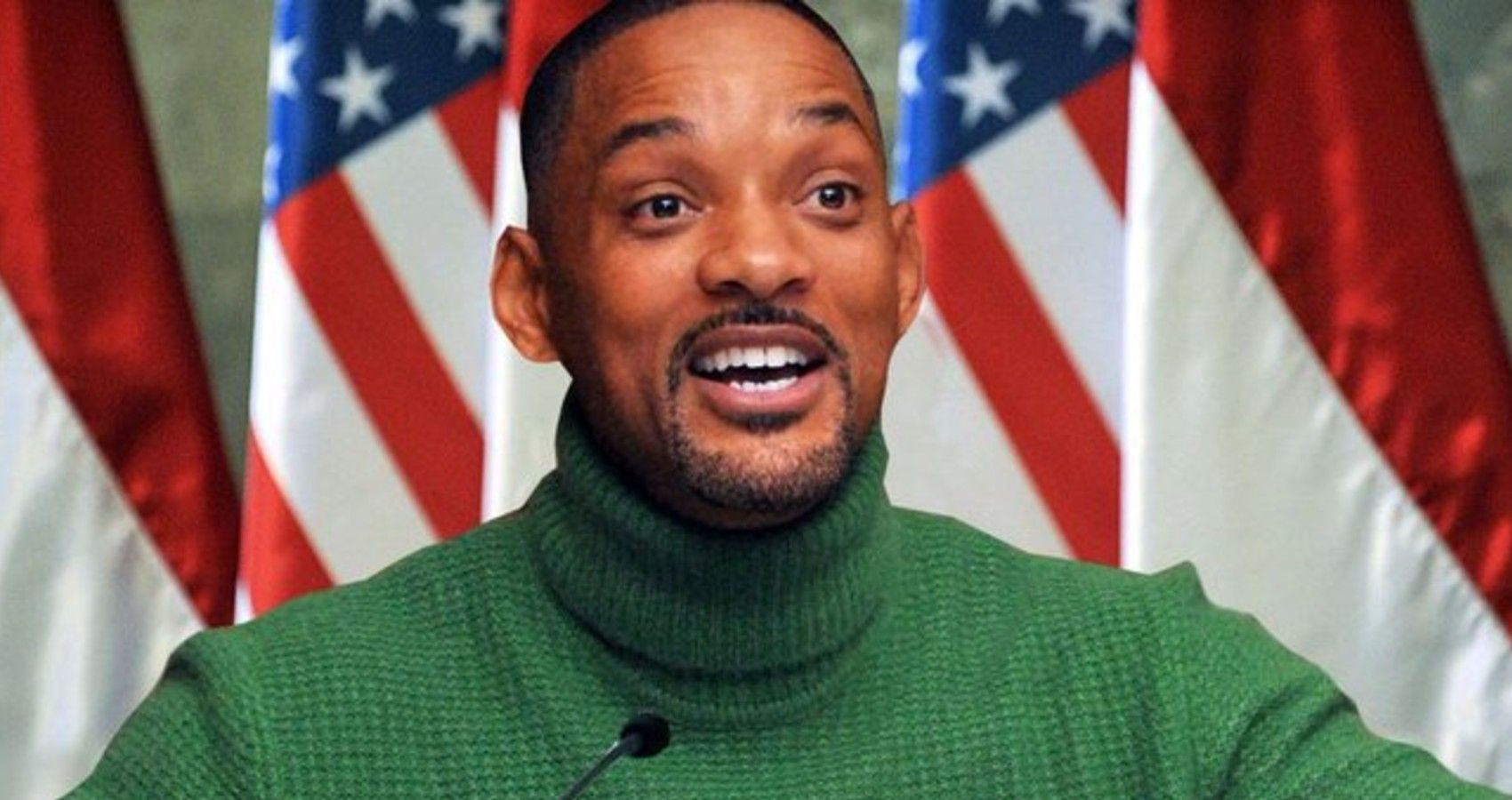 Will Smith in green sweater talking in front of American flags