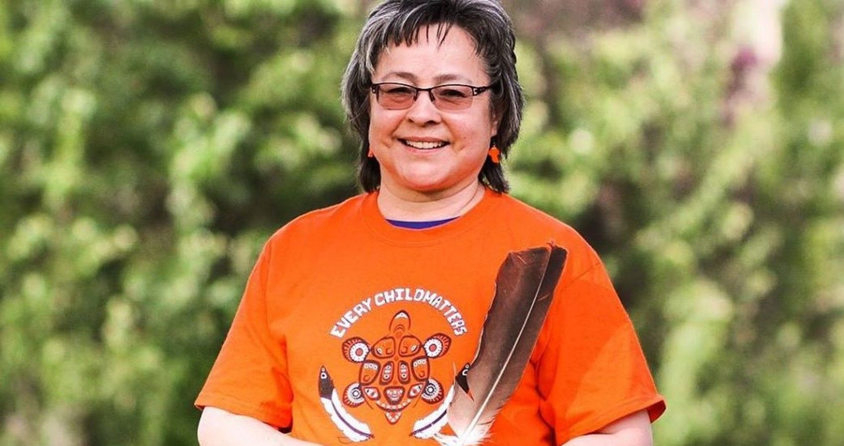 Phyllis Webstad standing in an orange shirt holding a feather