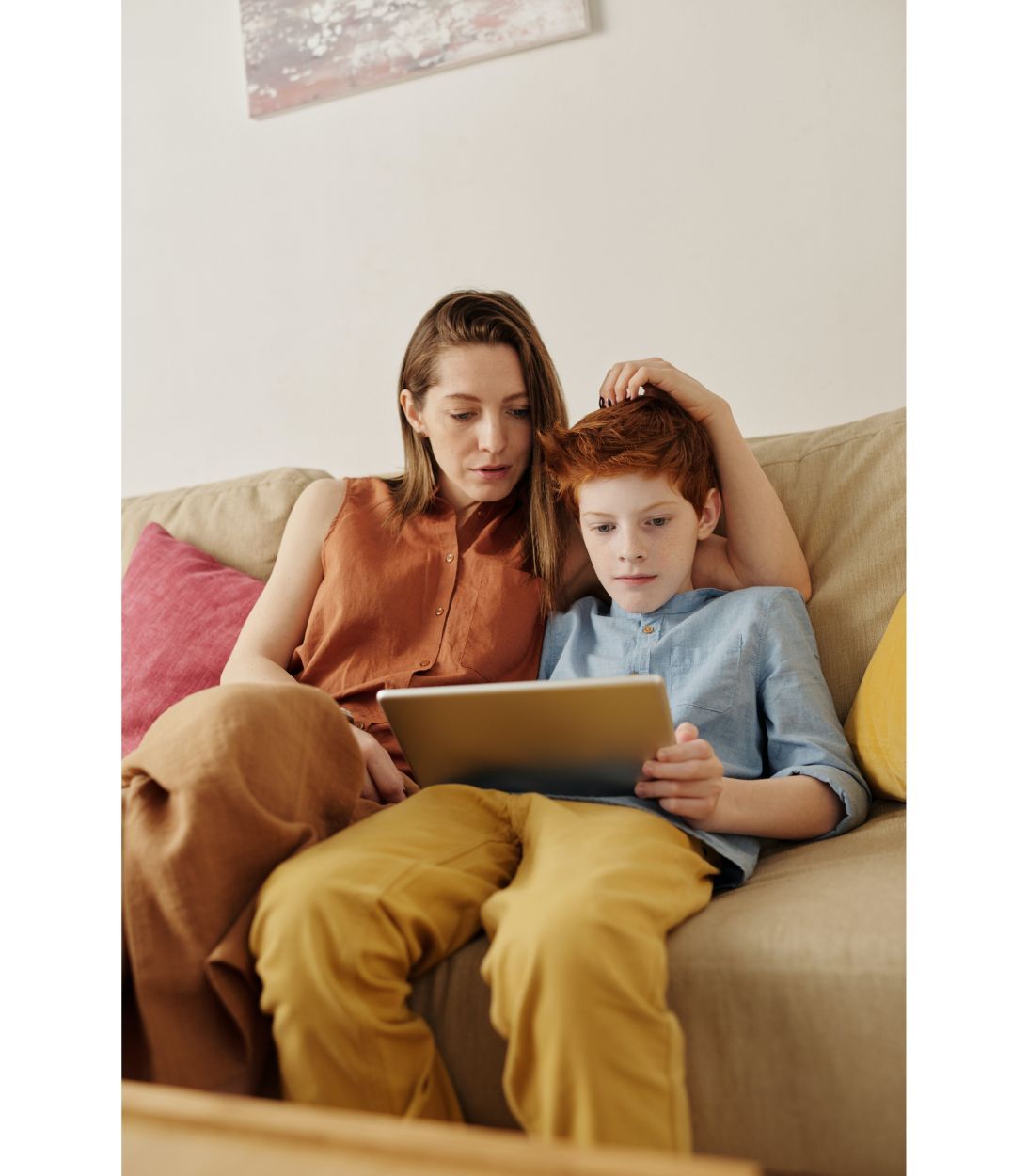 A mom and her son sitting on the couch looking at the tablet