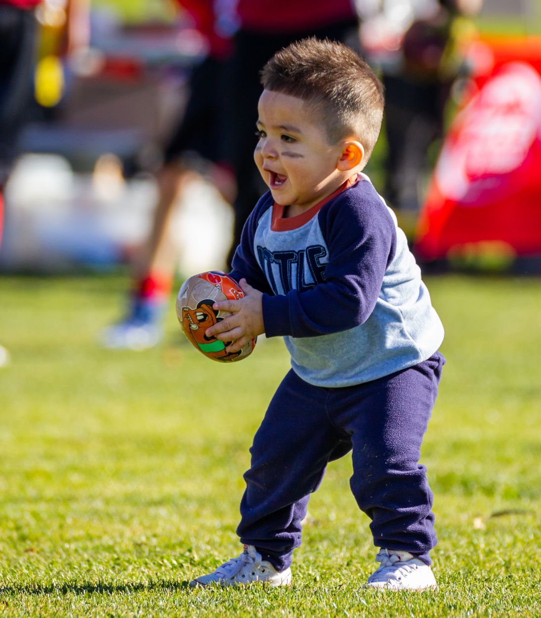 A small boy holding a ball while standing on the field.