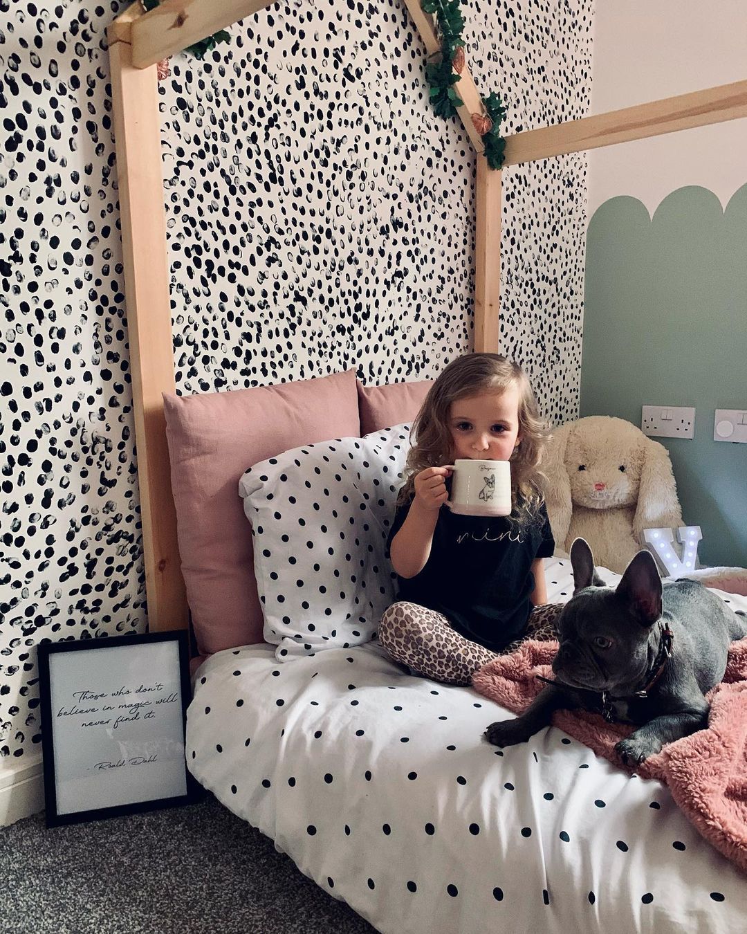 A child sitting on her bed with a cup and her dog
