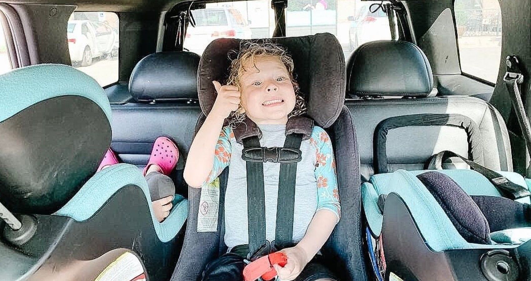 A child in her car seat giving a thumbs up