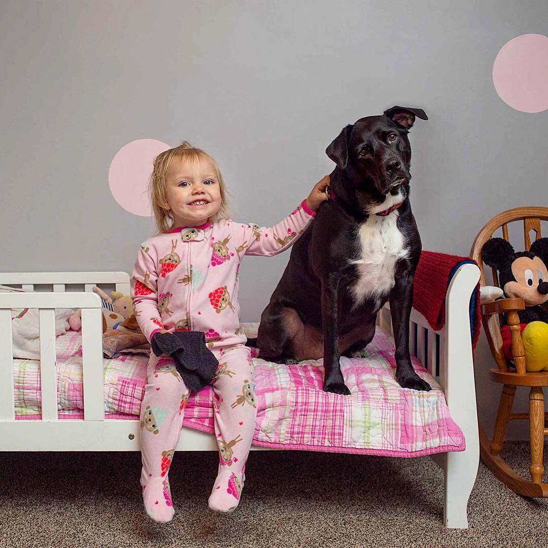 A child sitting on her bed with her dog and looking happy