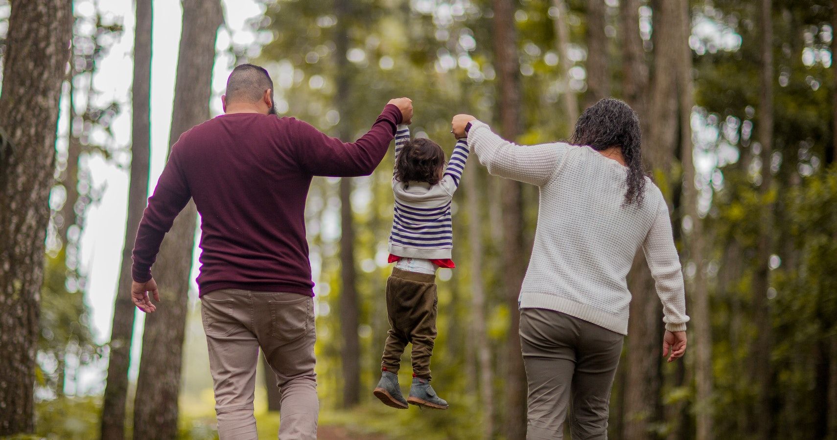 Parents Both Holding Child Up In Woods