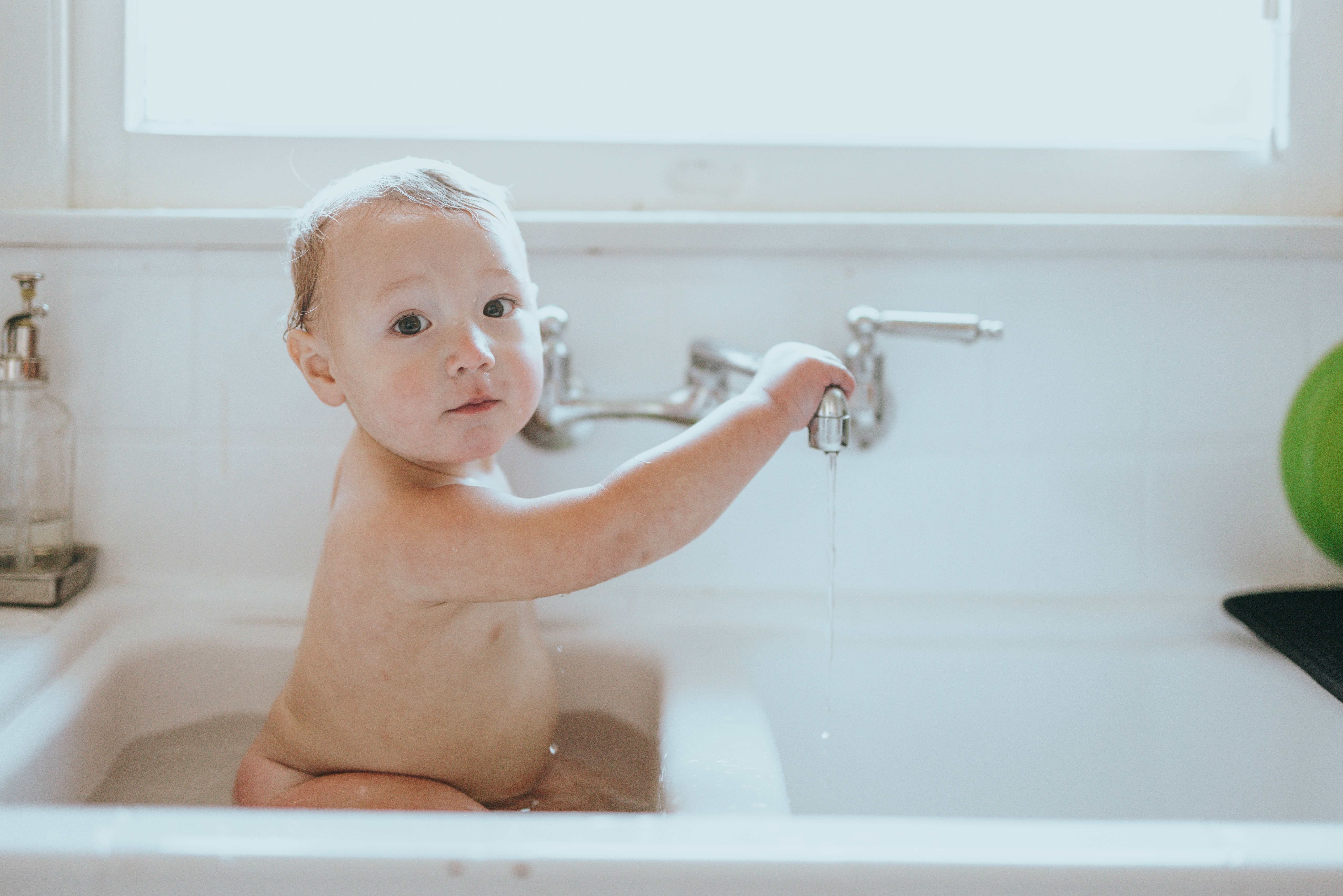 A baby sitting in the sink having a bath