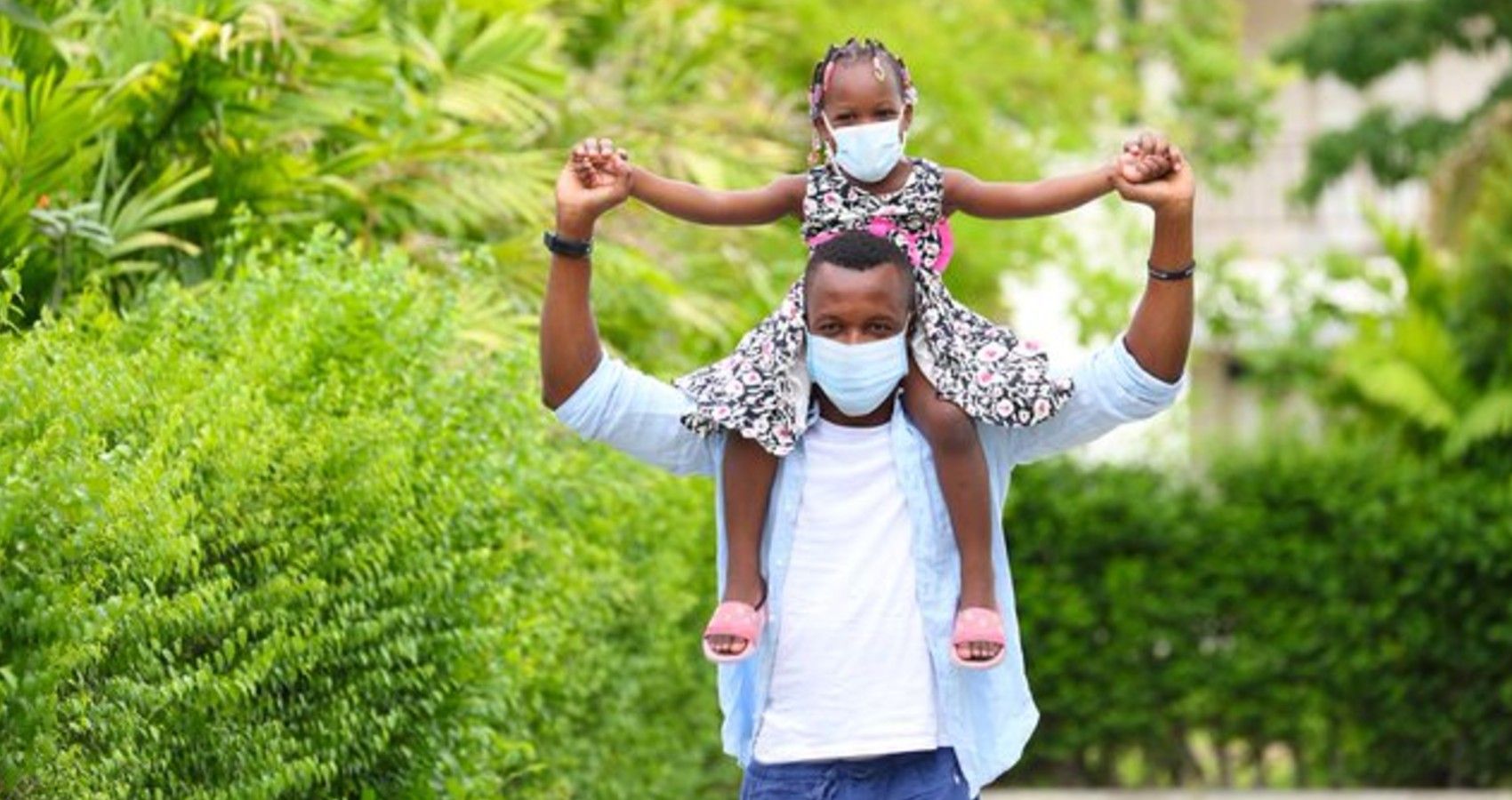 A dad holding his daughter on his shoulders and they are wearing face masks