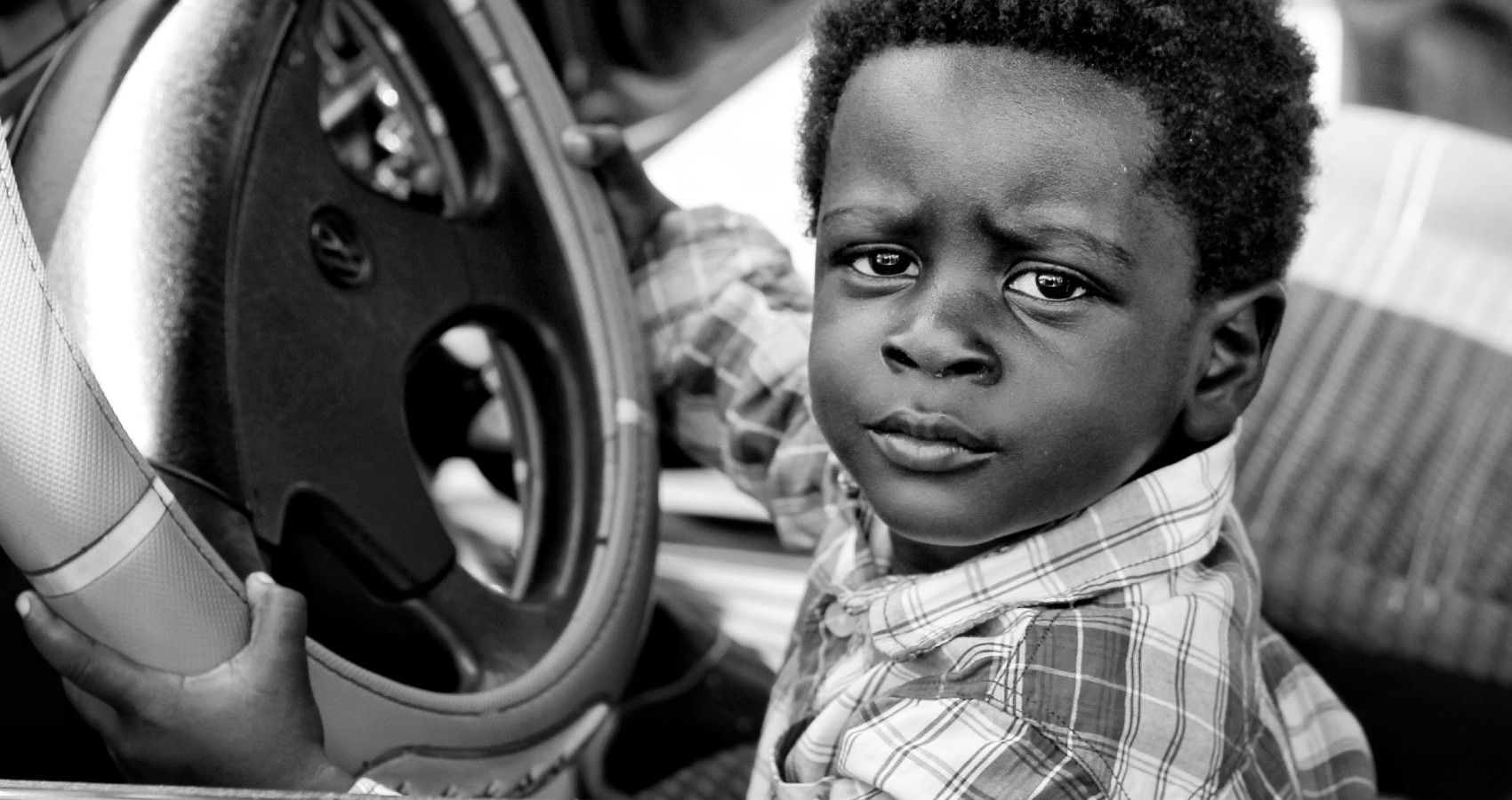 A small boy sitting in the front seat of the car at the steering wheel