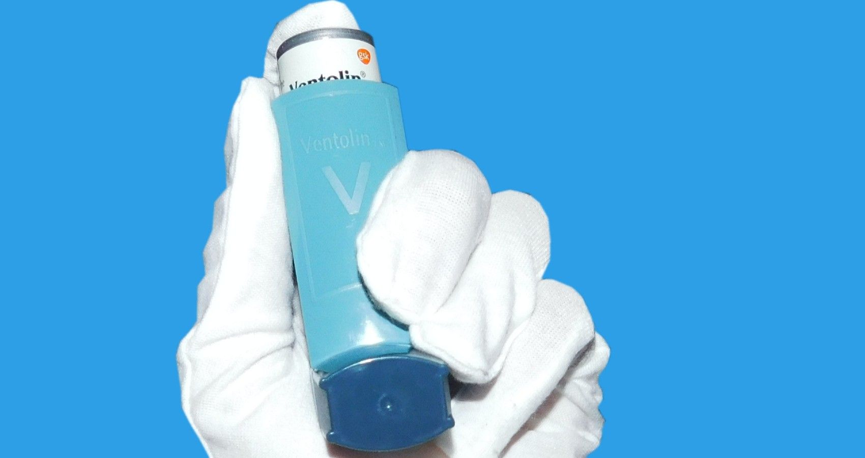 A gloved hand holding an asthma inhaler