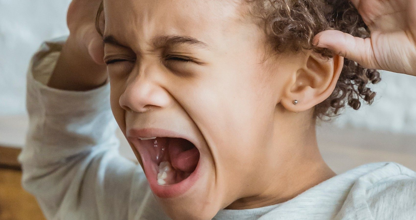 A child screaming with their hands on their ears