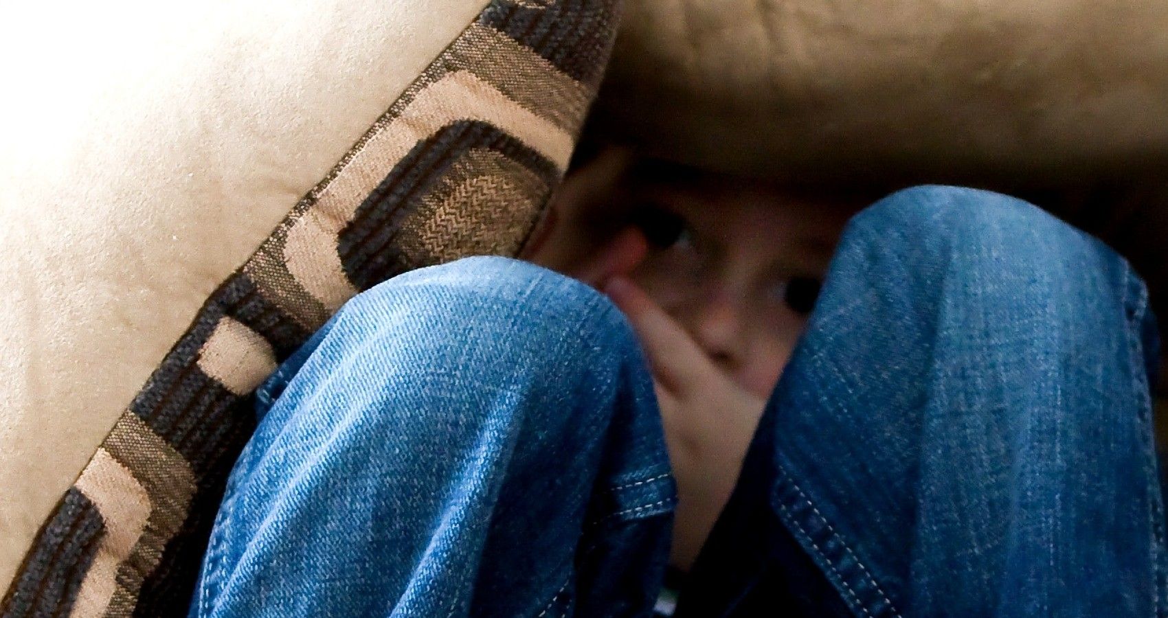 A child sitting on the couch under some pillows