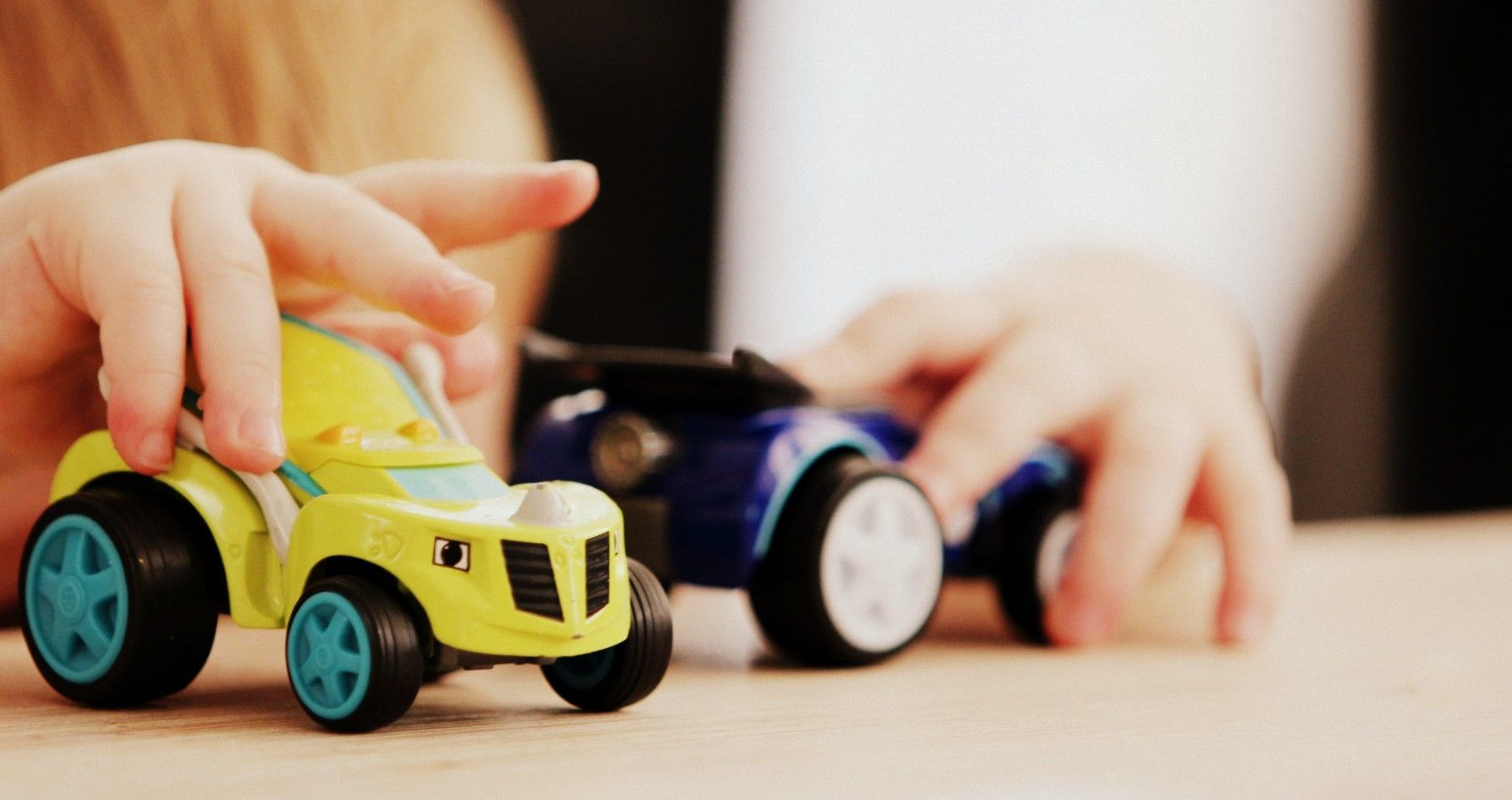 A Boy Playing With Two Plastic Cars