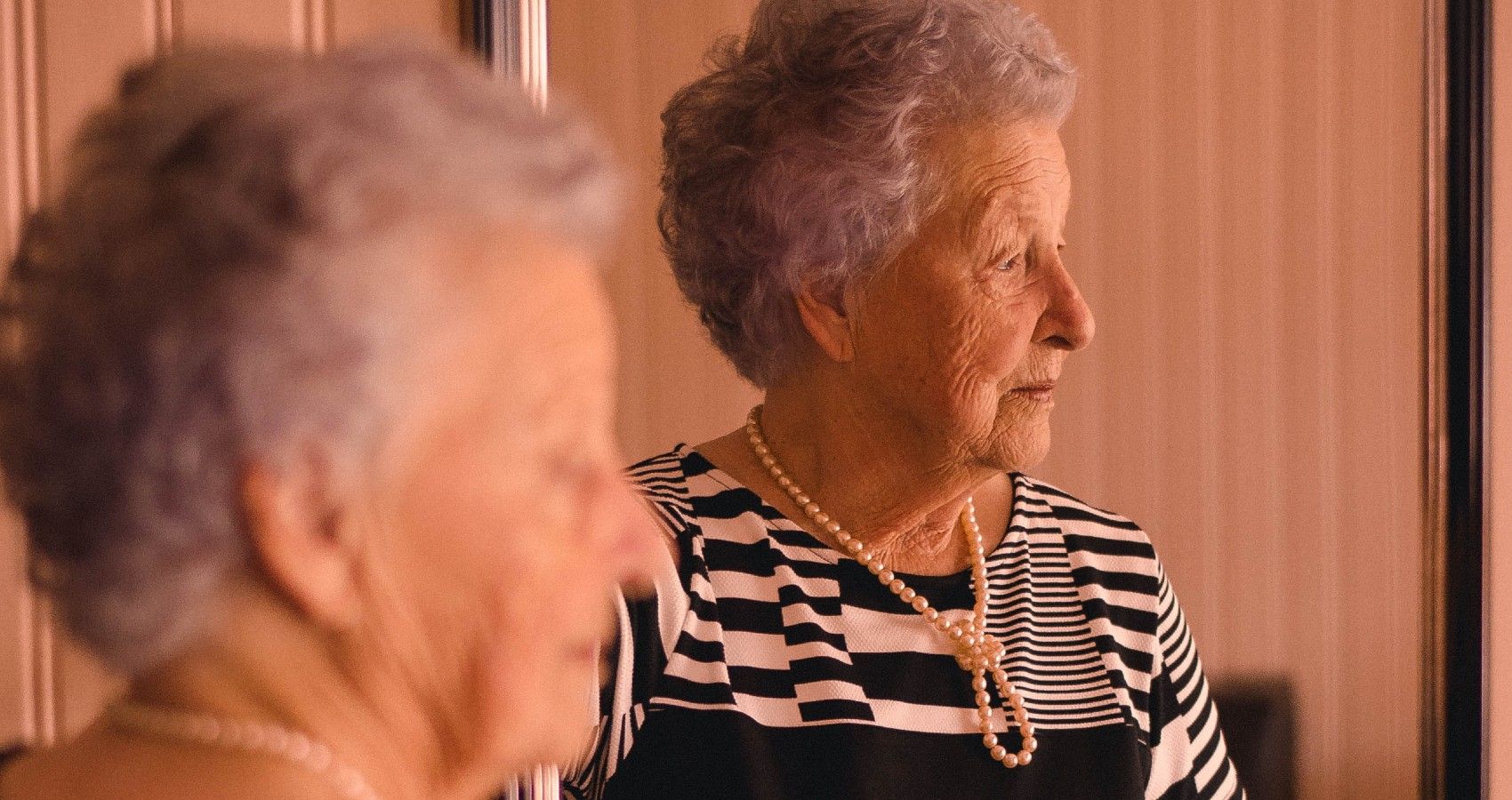 An Older Woman Looking In A Mirror And Looks Sad