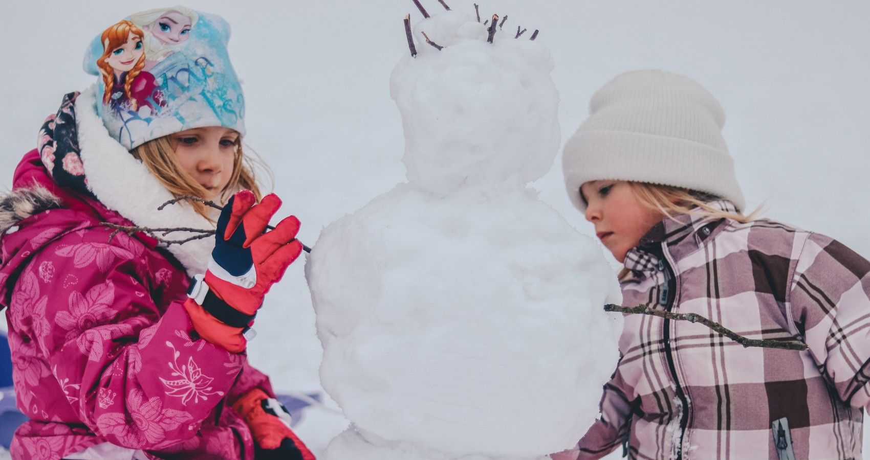 Two Young Girls In Snowsuits Playing Out In Snow