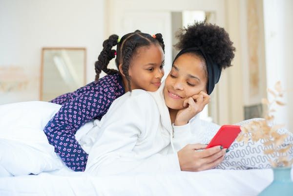 Mom on bed looking at her phone with daughter