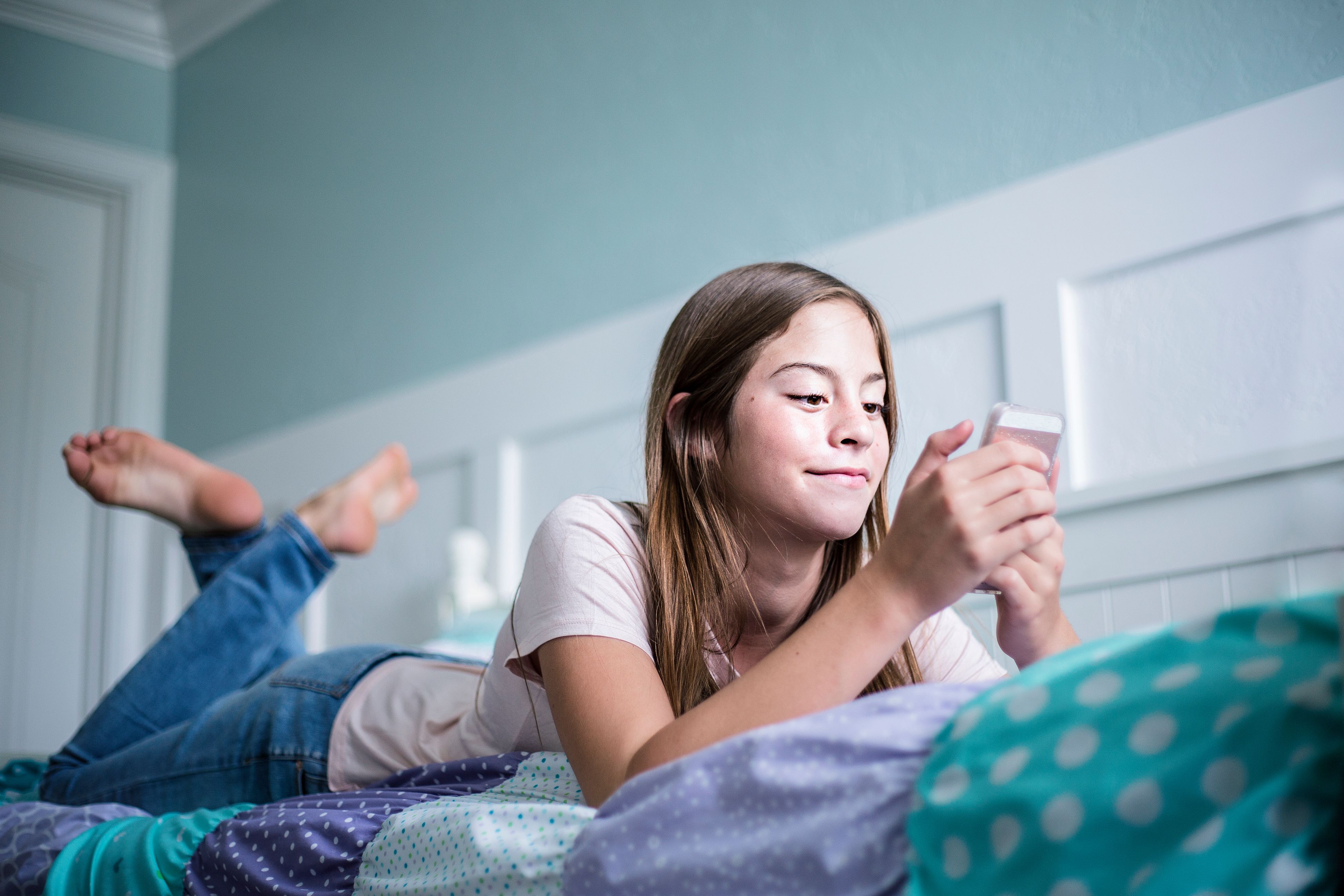 teen girl lying in bed on phone